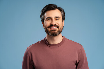 Smiling bearded man wearing casual posing in studio isolated on blue, looking at camera