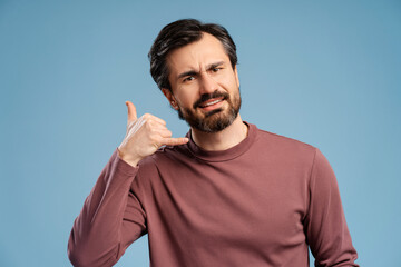 Young man doing phone finger gesture like call posing in studio looking at camera