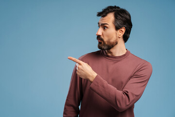 Portrait of bearded man wearing stylish casual clothes and pointing fingers to copy space