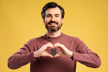 Portrait of smiling man holding pacemaker in two hands, isolated in yellow background