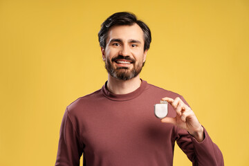 Portrait of attractive man holding pacemaker in hand, isolated in yellow background