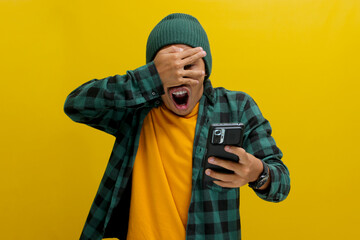 Shocked Asian man, dressed in a beanie hat and casual shirt, covers his eyes in a comical and...
