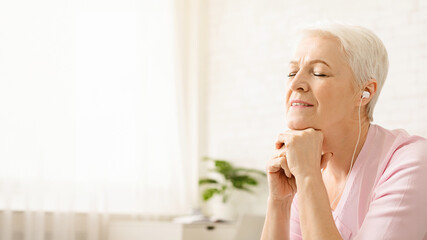 Time for relax. Serene senior woman enjoying peaceful music at home with closed eyes, empty space