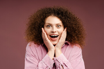 Beautiful overjoyed woman with curly hair surprised with open mouth looking at camera