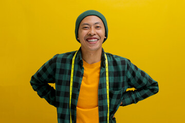Cheerful Asian man in a beanie and casual shirt smiles at the camera, holding a yellow measuring...