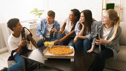 A group of teenagers sitting around a table, enjoying slices of pizza. The friends are engaged in...