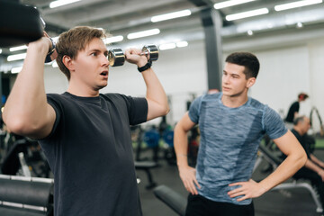 Portrait motivated sportsman working out with dumbbell with personal fitness trainer at gym. Sporty guy doing weight exercises with assistance of coach at sport club. Concept of healthy lifestyle.