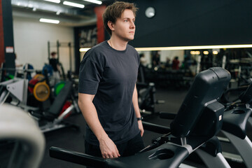 Portrait of male beginner wearing outfit walking on treadmill, working on health and fitness in gym. Athletic young man warming-up run routine exercise at sport club. Concept of healthy lifestyle