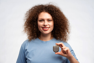 Attractive woman with curly hair in blue t shirt holding pacemaker in hand, looking at camera