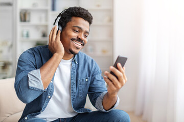 African American man is wearing headphones while engaged in a phone conversation on his cell phone....