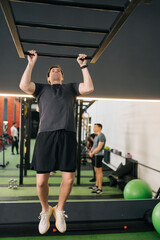 Vertical shot of beginner sportsman doing pull-ups on horizontal bar at gym. Sports male workout exercising. Fit and athletic man performing hands, arms, shoulder workout. Concept of healthy life.