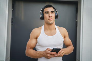 Portrait of young man outdoor use headphones and smart phone to play music or watch video podcast