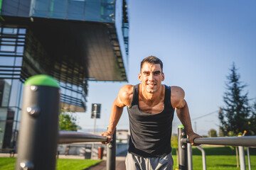 One man muscular male athlete training dips outdoor in sunny day