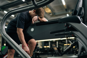 Tired runner male resting after jogging on treadmill during cardio session in gym. Satisfied fit young man standing on treadmill in fitness gym, feeling exhausted. Concept of healthy sports life.