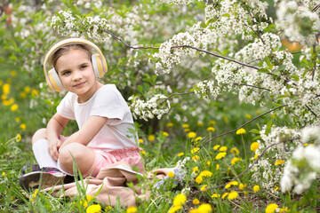 Generation Alpha. Happy child girl boy  headphones listens to music in a blossoming garden....