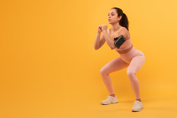 A young woman, dressed in activewear, is captured mid-motion as she performs a squat exercise,...