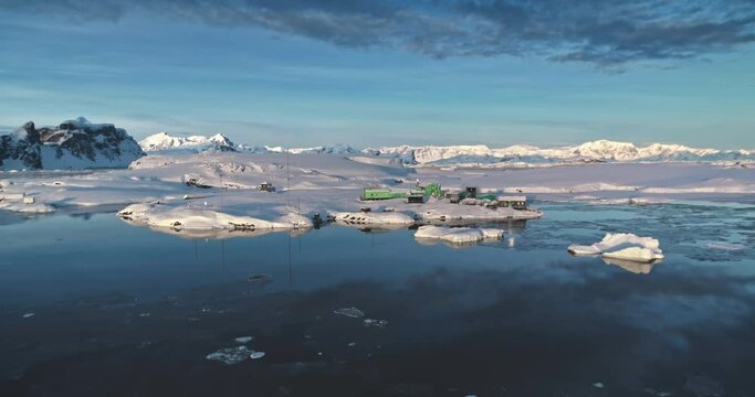 Aerial drone shot Antarctica polar base Vernadsky. Stunning wild nature winter sunset landscape. The snow covered land, mountains, cold ocean. A scientific research and weather station on South Pole