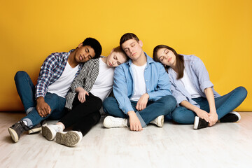 A diverse group of multiethnic teenagers are sitting closely on the floor, leaning on each other...