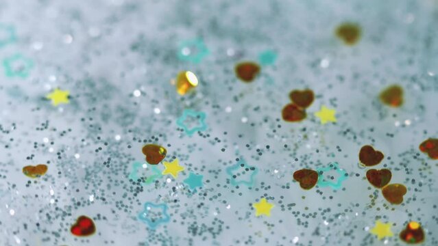 Decoration liquid. Shimmer fluid. Defocused gray yellow golden blue silver color stars figures sparkling crystal jeweled heart float sequins bokeh abstract art background.