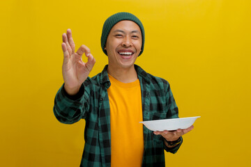 Asian man signals a delicious gesture with an OK sign while holding an empty plate, expressing...