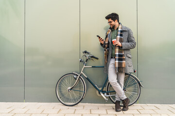 Handsome male business executive commuting to office on bicycle, checking his phone and having his...