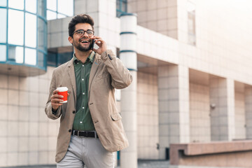Cheerful man with glasses having a phone call conversation while walking on the city street.
