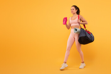 A young woman is dressed in workout attire, including a sports bra and leggings, carrying a black...