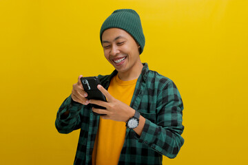 Happy and amazed Asian man, sporting a beanie hat and casual shirt, is using his smartphone for...