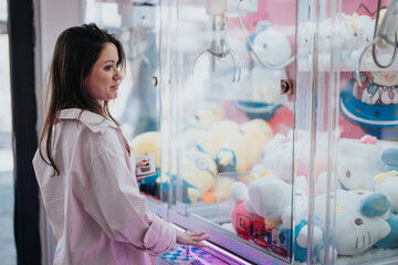 A young adult female is seen playing a claw crane game at an arcade, surrounded by colorful plush...