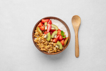 Natural yogurt with granola, kiwi and strawberries in a wooden bowl on a light background with spoon.