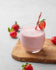 A glass of fresh strawberry smoothie on a wooden board on a light background with fresh berries.