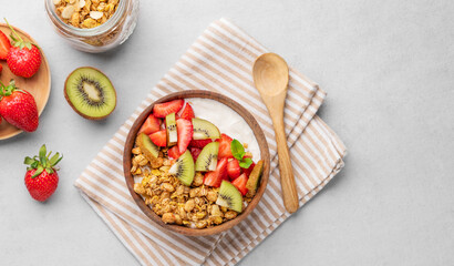 Natural yogurt with granola, kiwi and strawberries in a wooden bowl on a light background with fresh berries and fruits.