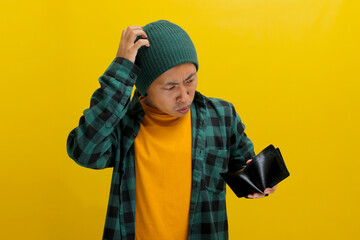 Broke Asian man dressed in a beanie hat and casual shirt, scratches his head in confusion as he...