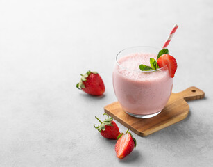 A glass of fresh strawberry smoothie with mint on a wooden board on a light background with fresh berries.