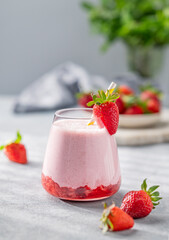 Strawberry milkshake or smoothie in a glass on a light background with fresh berries and shadows.