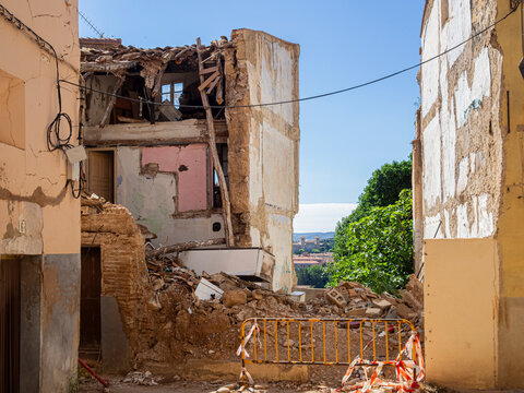 Vista de un edificio en ruinas con una valla amarilla de aviso, piedras  y restos de construcci&oacute;n con peligro de derrumbe. Verano de 2021 Espa&ntilde;a.