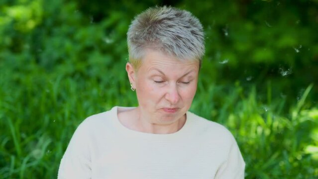 Caucasian woman sneezes and blows her nose into a paper napkin against a green background. Spring exacerbation of allergy to poplar fluff. Allergy in adults hay fever