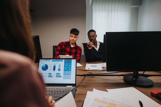 A diverse team of young businesspeople engaged in analyzing statistical data on a computer screen in a well-lit office environment.