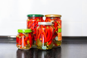 Pickled red hot hot chili peppers in jars on a black table. Canning vegetables.