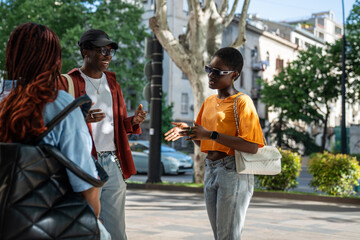 Joyful African American youths friends engaged in conversation while strolling city streets,...