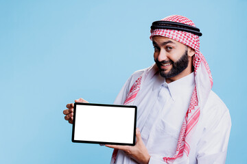 Cheerful muslim man offering digital tablet with empty screen mockup, advertising product portrait....