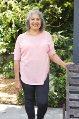 Senior biracial woman enjoying outdoors, leaning on bench, smiling