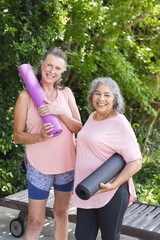 Outdoors, diverse senior female friends holding yoga mats, smiling
