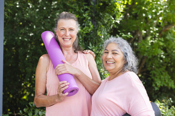 Enjoying outdoors, diverse senior female friends holding yoga mats, both smiling