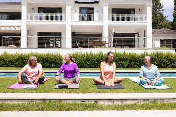 Outdoors, diverse senior female friends relaxing by pool, soaking up the sun