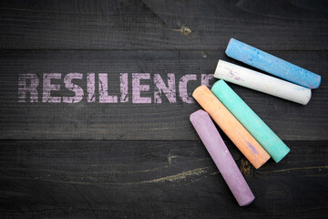 Resilience concept. Text and pieces of chalk on a dark wood texture background