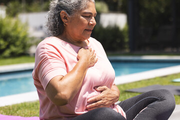 Outdoors, senior biracial woman practicing yoga by pool
