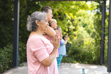 Diverse senior female friends do yoga outdoors, hands together