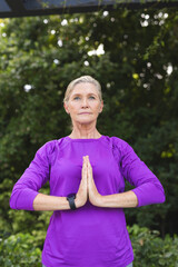 Practicing yoga outdoors, Caucasian senior female wears a purple top