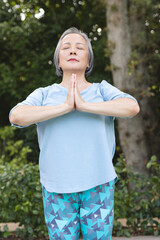 A senior Asian female practicing yoga outdoors with blue background